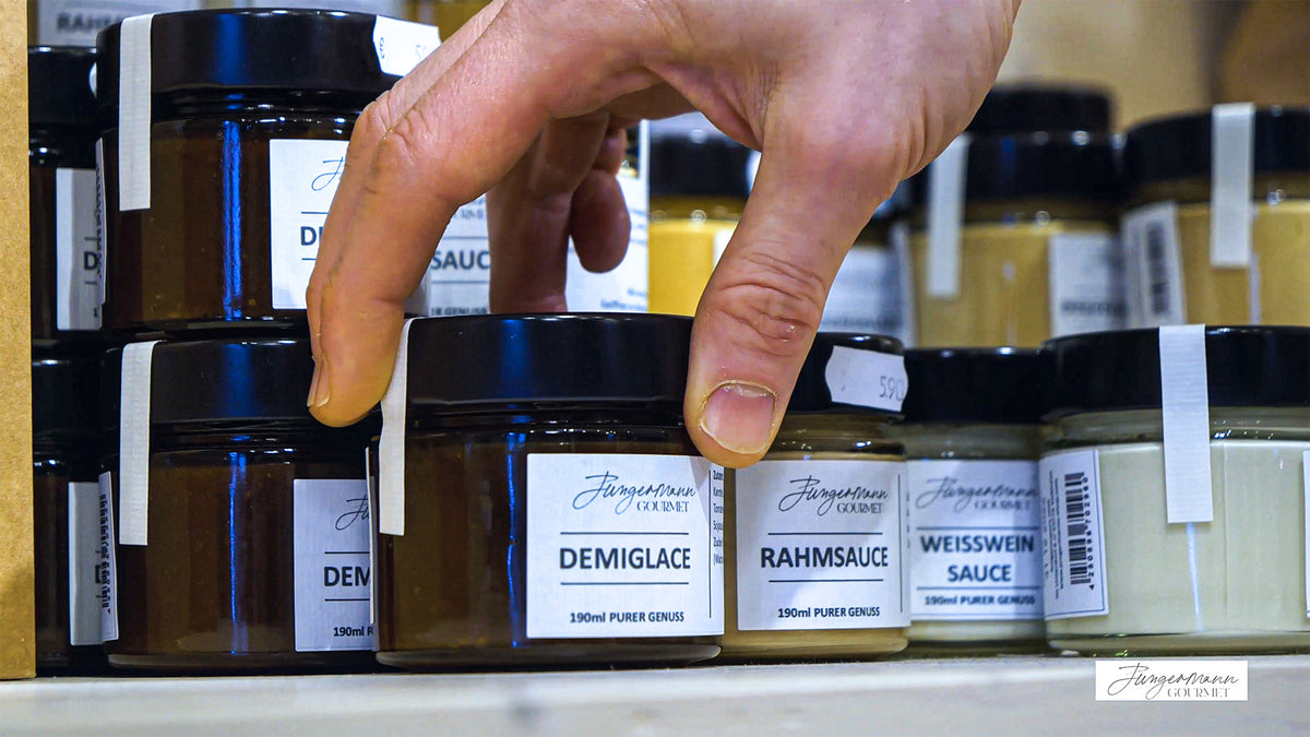 Hand greift im Jungermann-Gourmet-Ladengeschäft nach einem Glas Demiglace neben Rahm- und Weißweinsauce im Regal