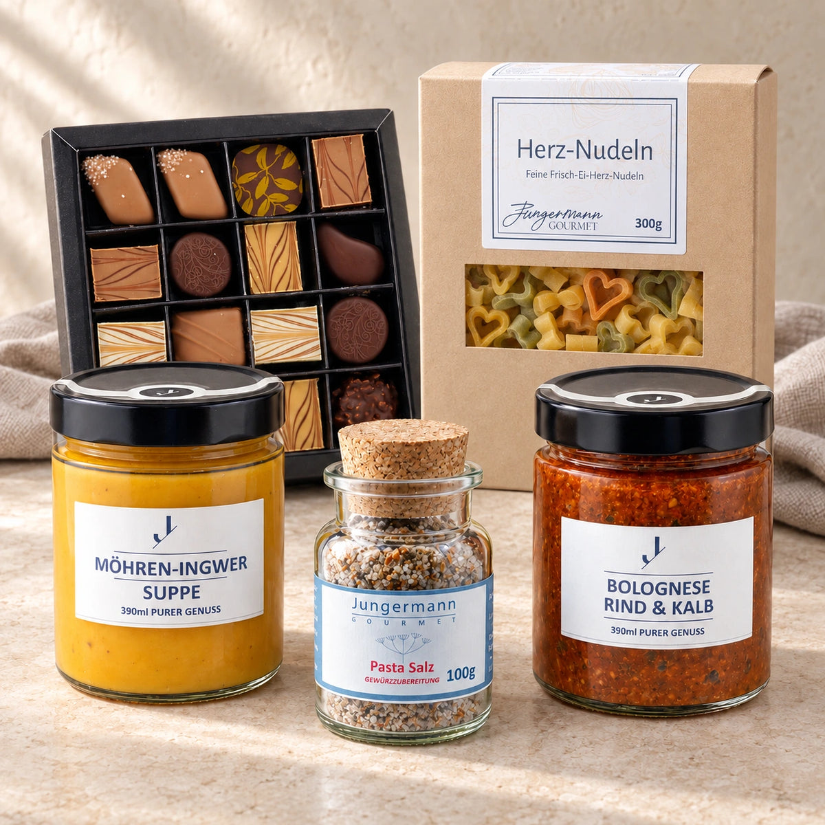 Abend zu zweit von Jungermann Gourmet mit Möhren-Ingwer-Suppe, Bolognese, Pasta-Salz, Herznudeln und Pralinen auf hellem Naturstein.