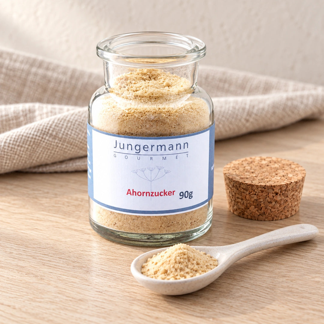 Geöffnetes Originalglas mit Ahorn-Zucker, daneben der Korkverschluss und ein Keramiklöffel mit hellbeigem Zucker.