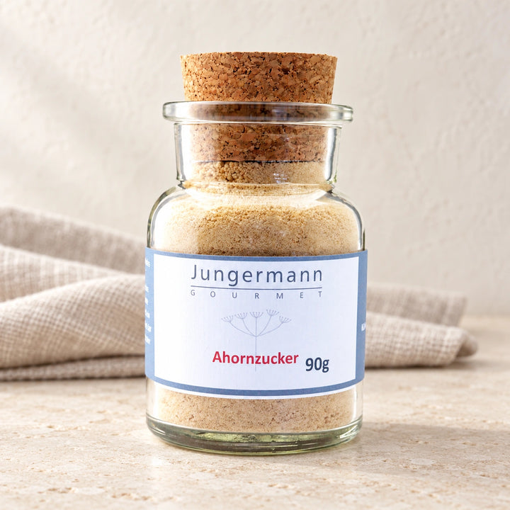 Ahorn-Zucker im originalen Korkglas mit blau gerahmtem Etikett auf hellem Naturstein.