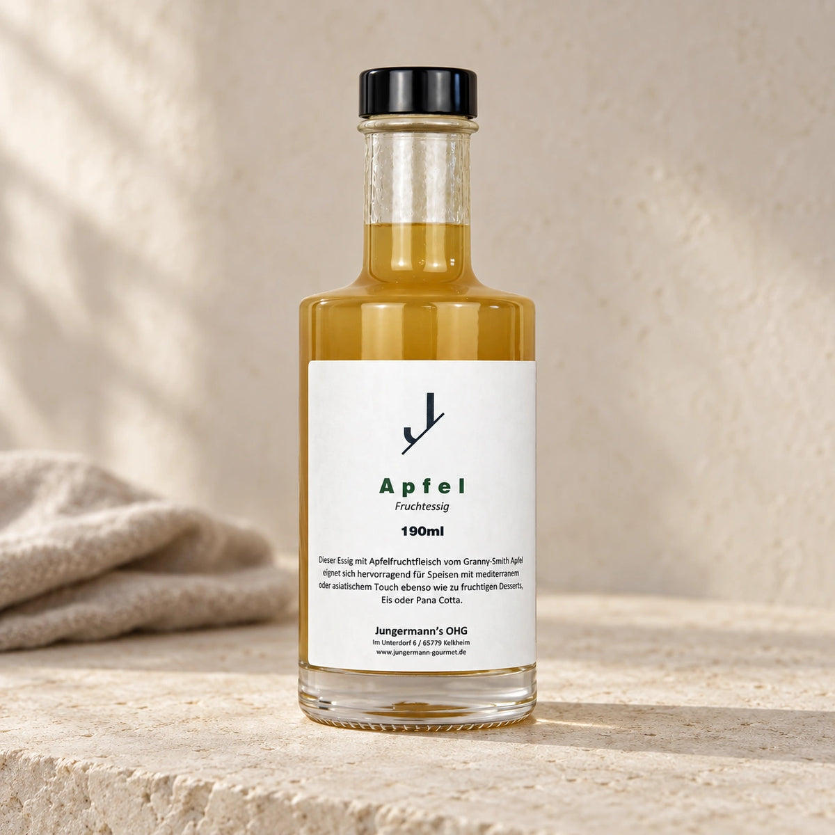 Apfel-Fruchtessig von Jungermann Gourmet in der Glasflasche mit schwarzem Verschluss und weißem Etikett auf hellem Naturstein.