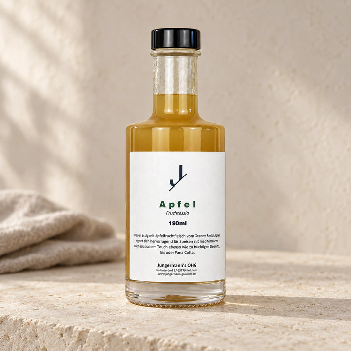 Apfel-Fruchtessig von Jungermann Gourmet in der Glasflasche mit schwarzem Verschluss und weißem Etikett auf hellem Naturstein.