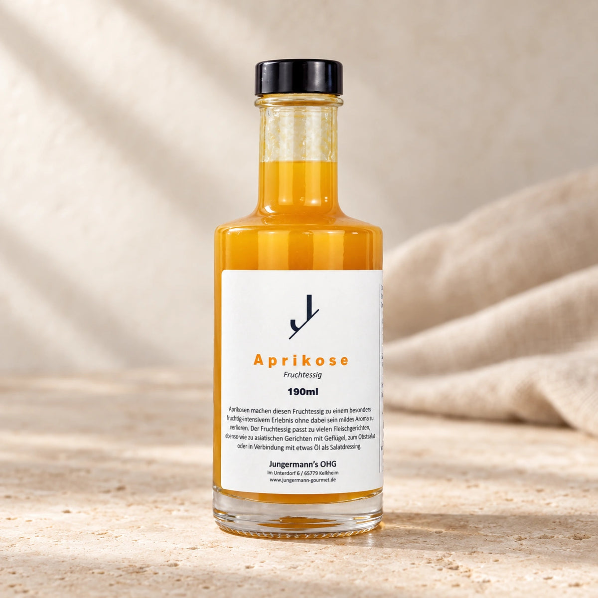 Aprikosen-Fruchtessig von Jungermann Gourmet in der Glasflasche mit schwarzem Verschluss und weißem Etikett auf hellem Naturstein.