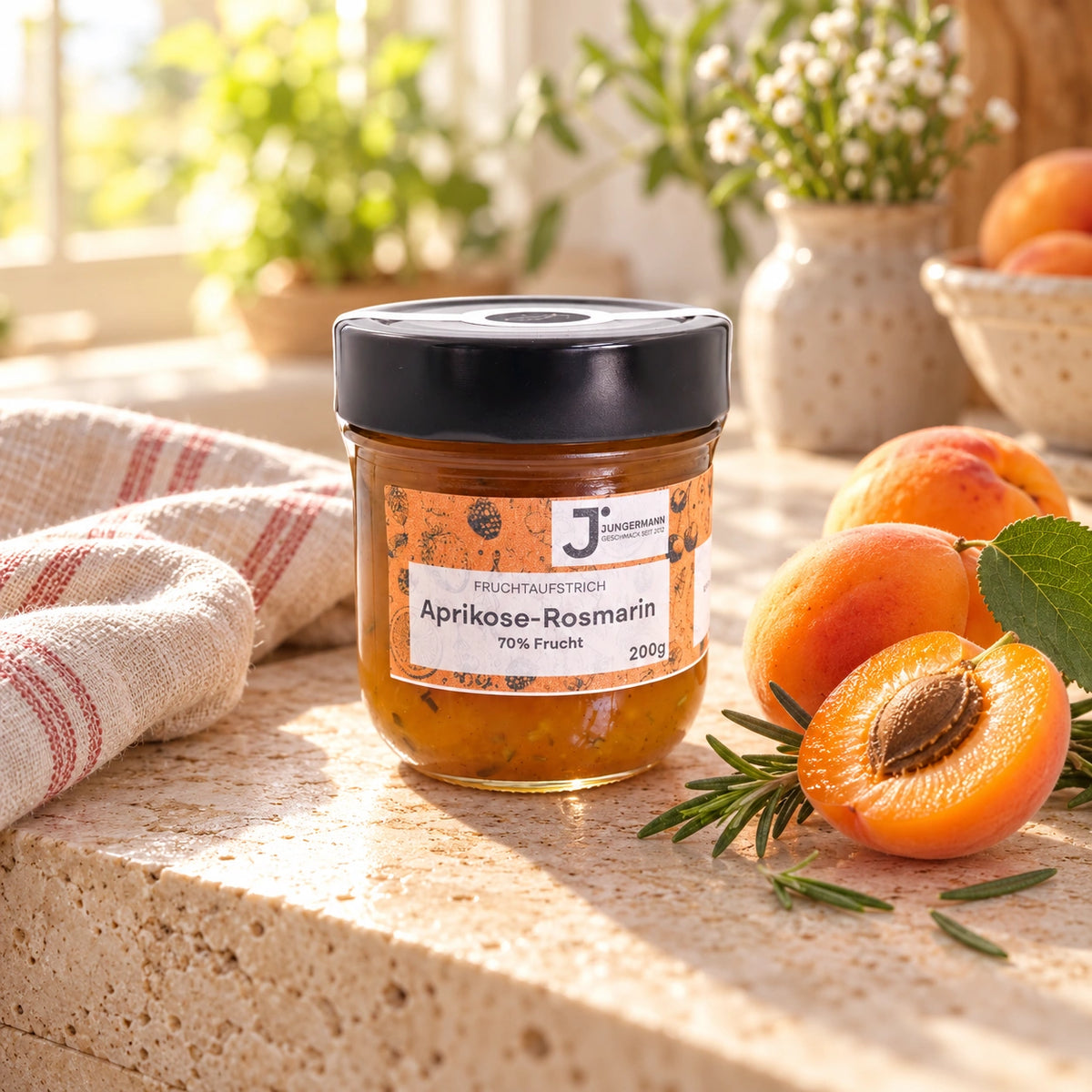 Aprikosen-Rosmarin Fruchtaufstrich von Jungermann Gourmet im 200-g-Glas auf hellem Naturstein mit halbierten Aprikosen und frischem Rosmarin