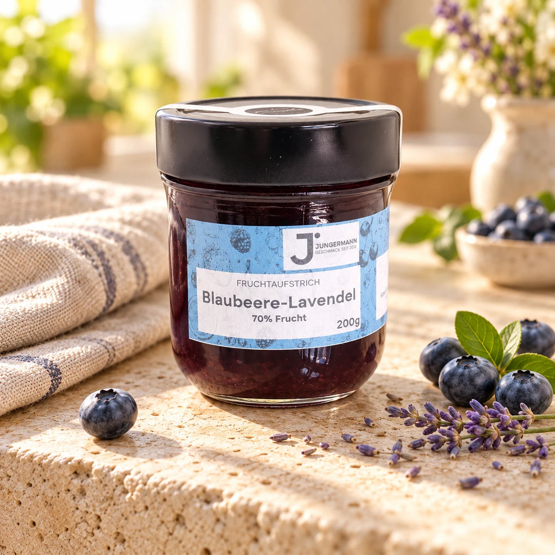 Blaubeere-Lavendel Fruchtaufstrich von Jungermann Gourmet im 200-g-Glas auf hellem Naturstein mit frischen Blaubeeren und Lavendelblüten