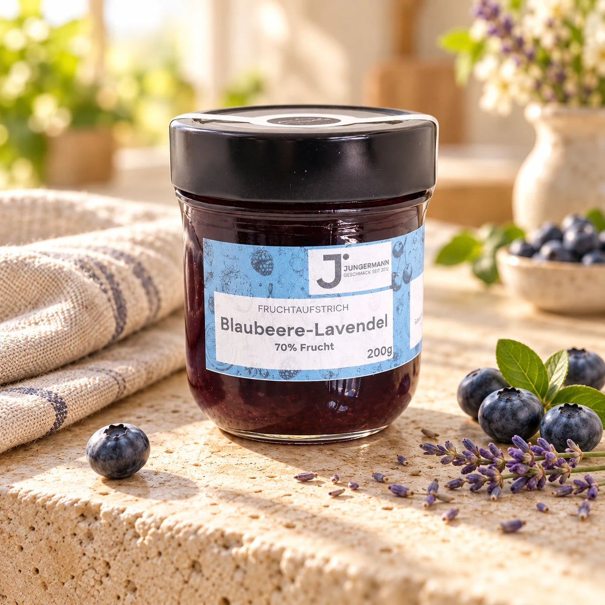 Blaubeere-Lavendel Fruchtaufstrich von Jungermann Gourmet im 200-g-Glas auf hellem Naturstein mit frischen Blaubeeren und Lavendelblüten