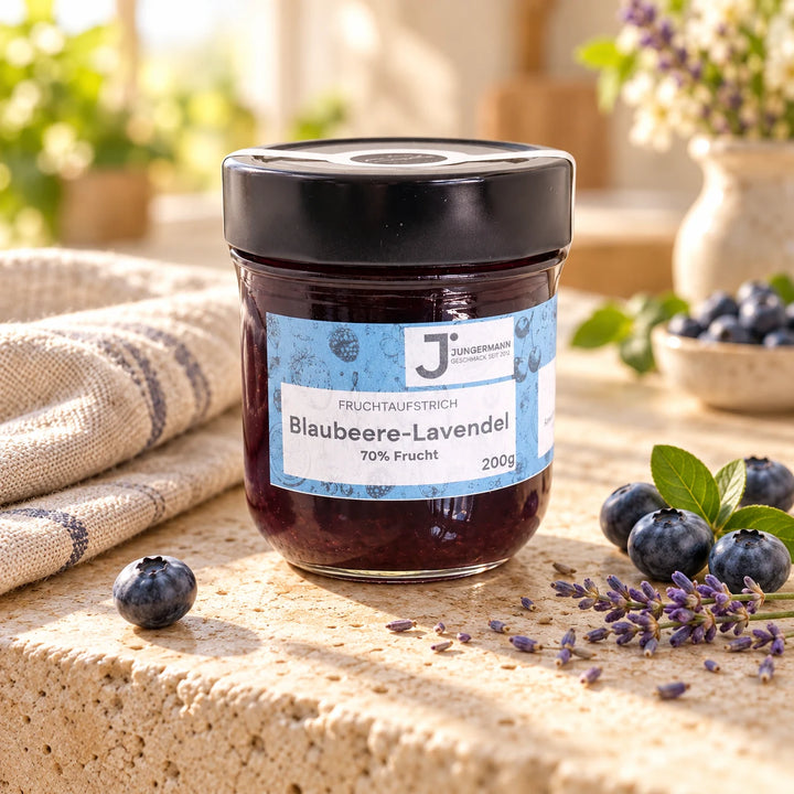 Blaubeere-Lavendel Fruchtaufstrich von Jungermann Gourmet im 200-g-Glas auf hellem Naturstein mit frischen Blaubeeren und Lavendelblüten