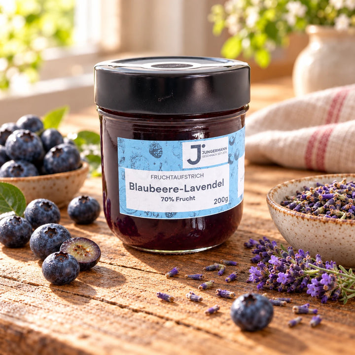Blaubeere-Lavendel Fruchtaufstrich im Originalglas auf rustikalem Holz mit frischen Blaubeeren und Lavendelblüten als Zutaten