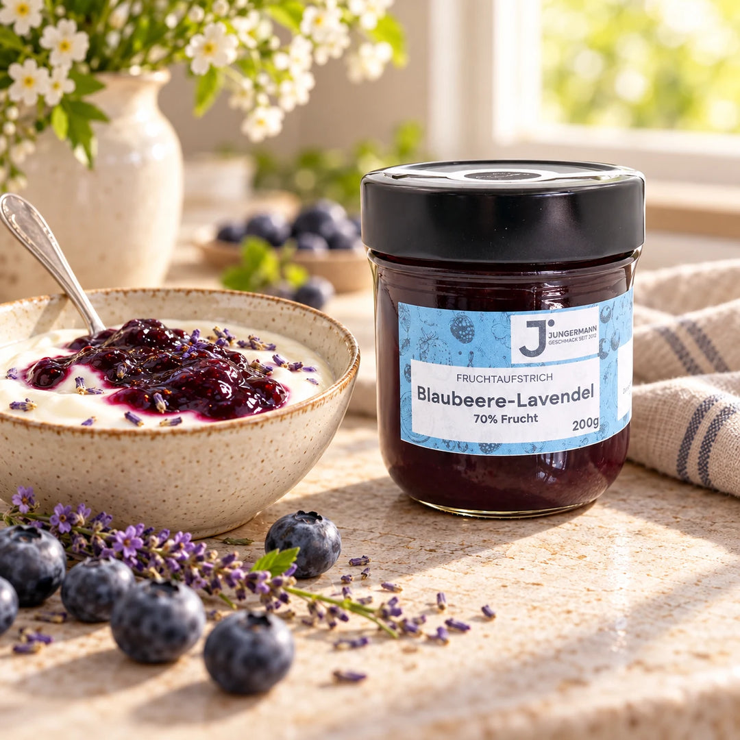 Serviervorschlag: Naturjoghurt mit Blaubeere-Lavendel Fruchtaufstrich in einer Keramikschale neben dem Glas und frischen Blaubeeren