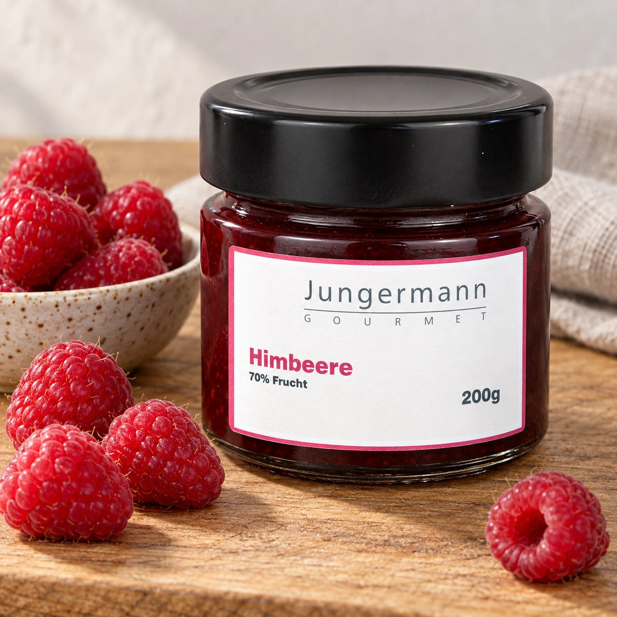 Himbeer-Aufstrich im 200-g-Originalglas neben frischen Himbeeren auf einem Holzbrett.