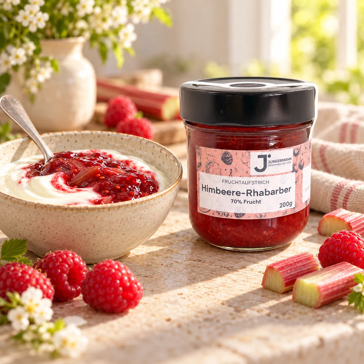 Serviervorschlag: Naturjoghurt mit Himbeere-Rhabarber Fruchtaufstrich in einer Keramikschale neben dem Glas und frischen Himbeeren