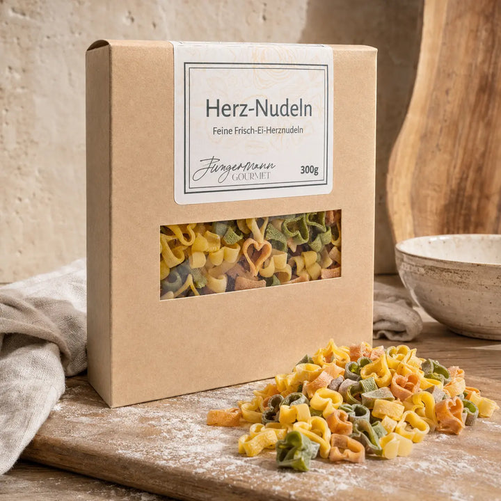 Mehrfarbige Frisch-Ei Herz-Nudeln mit Schachtel auf Holz