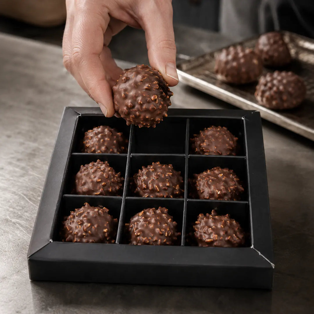 Haselnuss Pralinen beim Einlegen in die schwarze 3×3-Schachtel