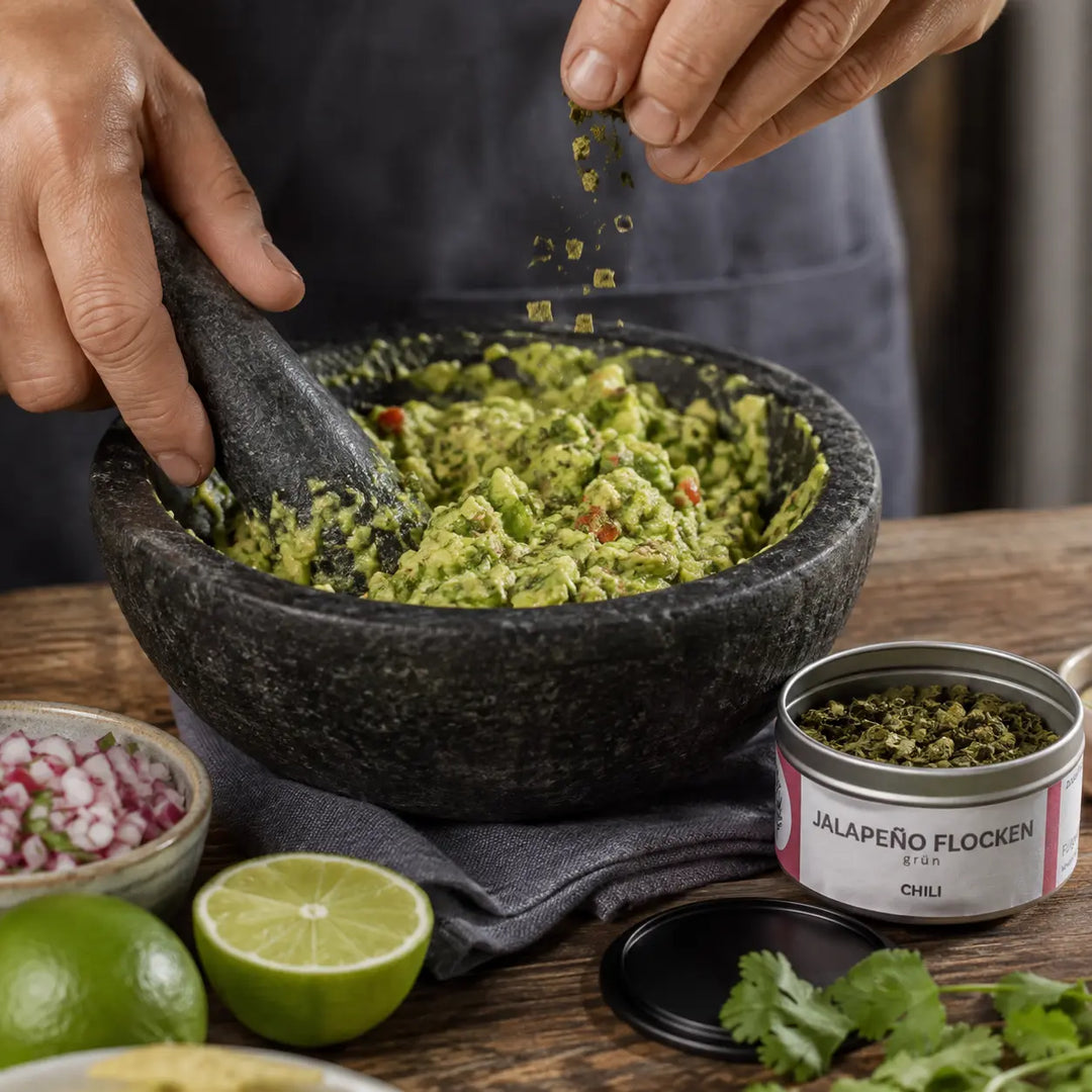 Grüne Jalapenoflocken beim Würzen von Guacamole