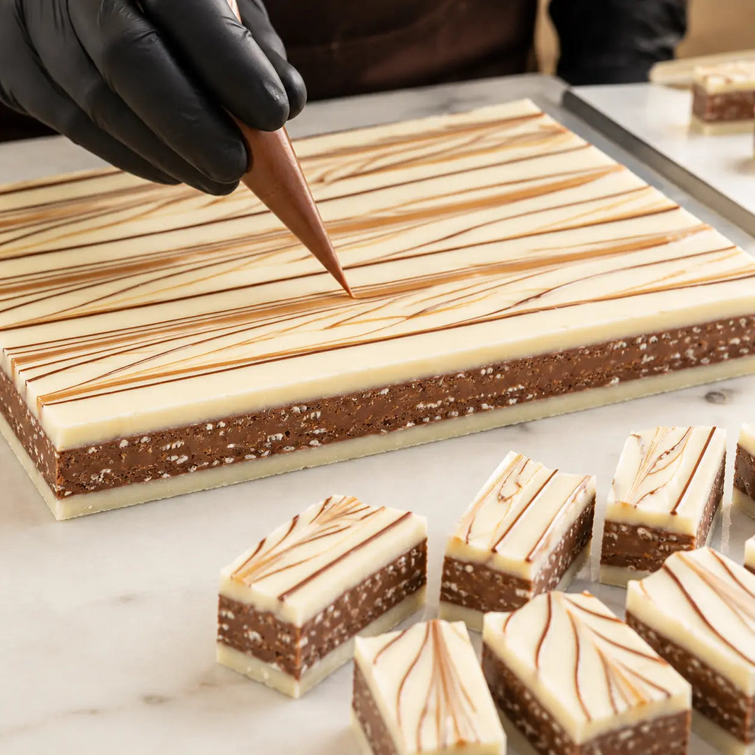 Weiße Knusper-Praline beim Verzieren mit dunklen und karamellfarbenen Schokoladenlinien