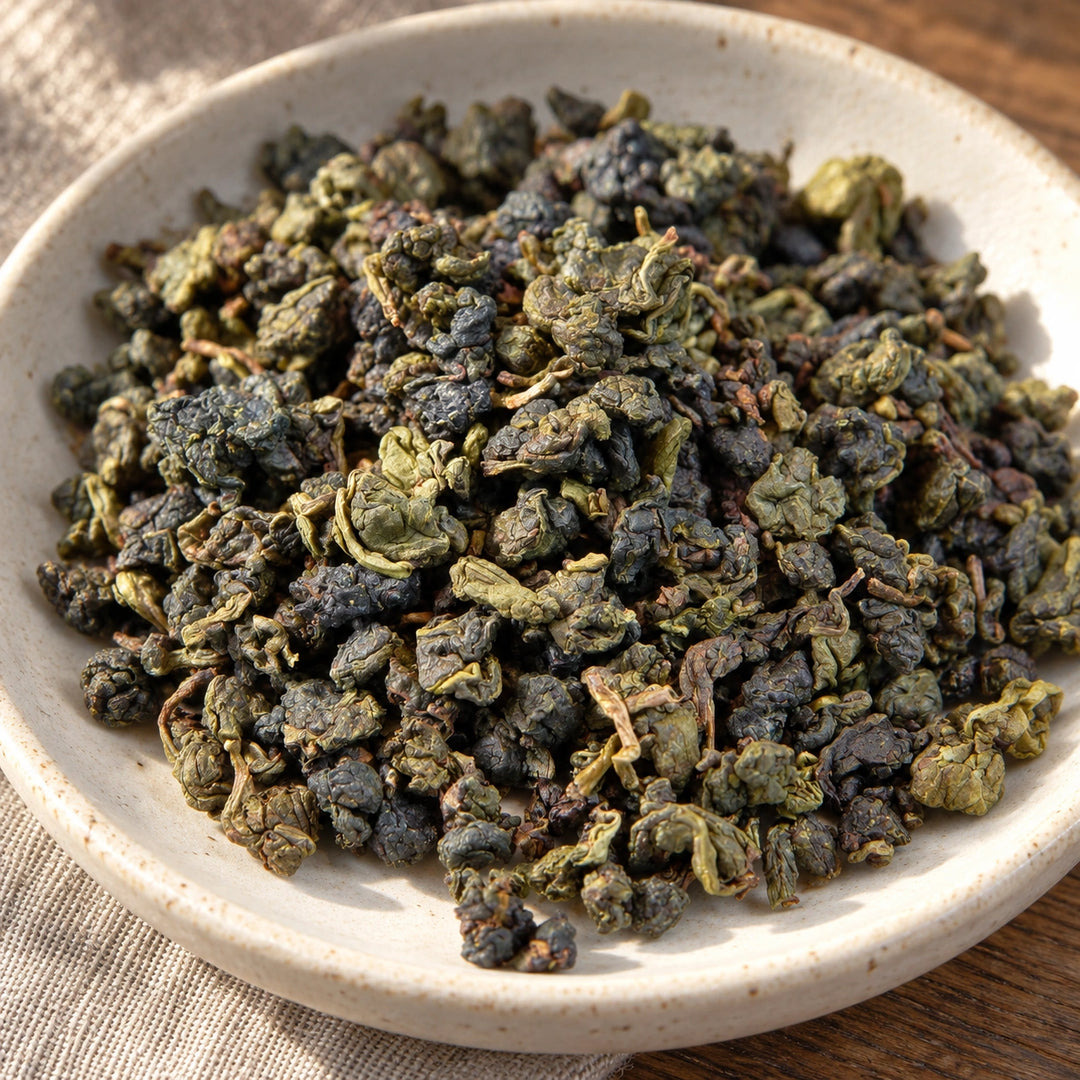 Nahaufnahme der unregelmäßig gerollten Jade-Oolong-Teeblätter in einer flachen Keramikschale.