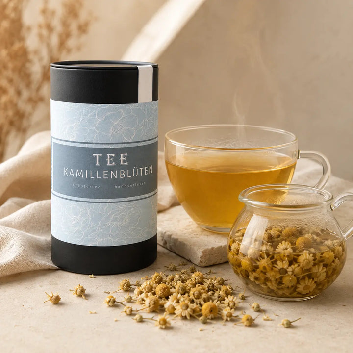 Kamillenblüten Tee mit dampfender Tasse, Glaskanne und getrockneten Blüten