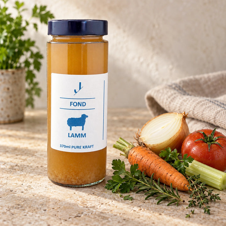 Lamm-Fond im originalen 370-ml-Glas neben Karotte, Zwiebel, Sellerie, Tomate, Petersilie, Rosmarin und Thymian.