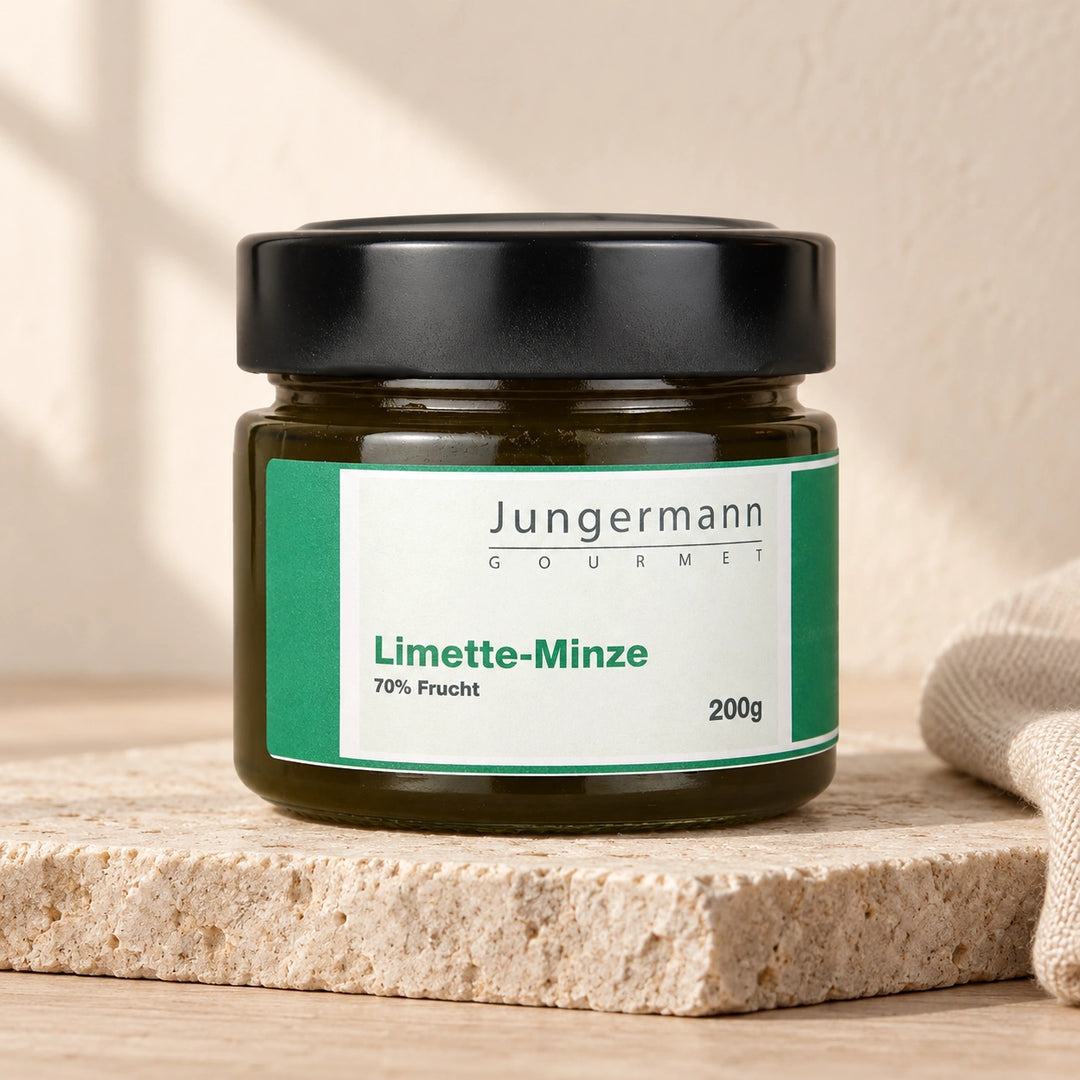 Limette-Minze-Aufstrich von Jungermann Gourmet im geschlossenen 200-g-Glas auf hellem Naturstein vor einer warm beleuchteten Wand