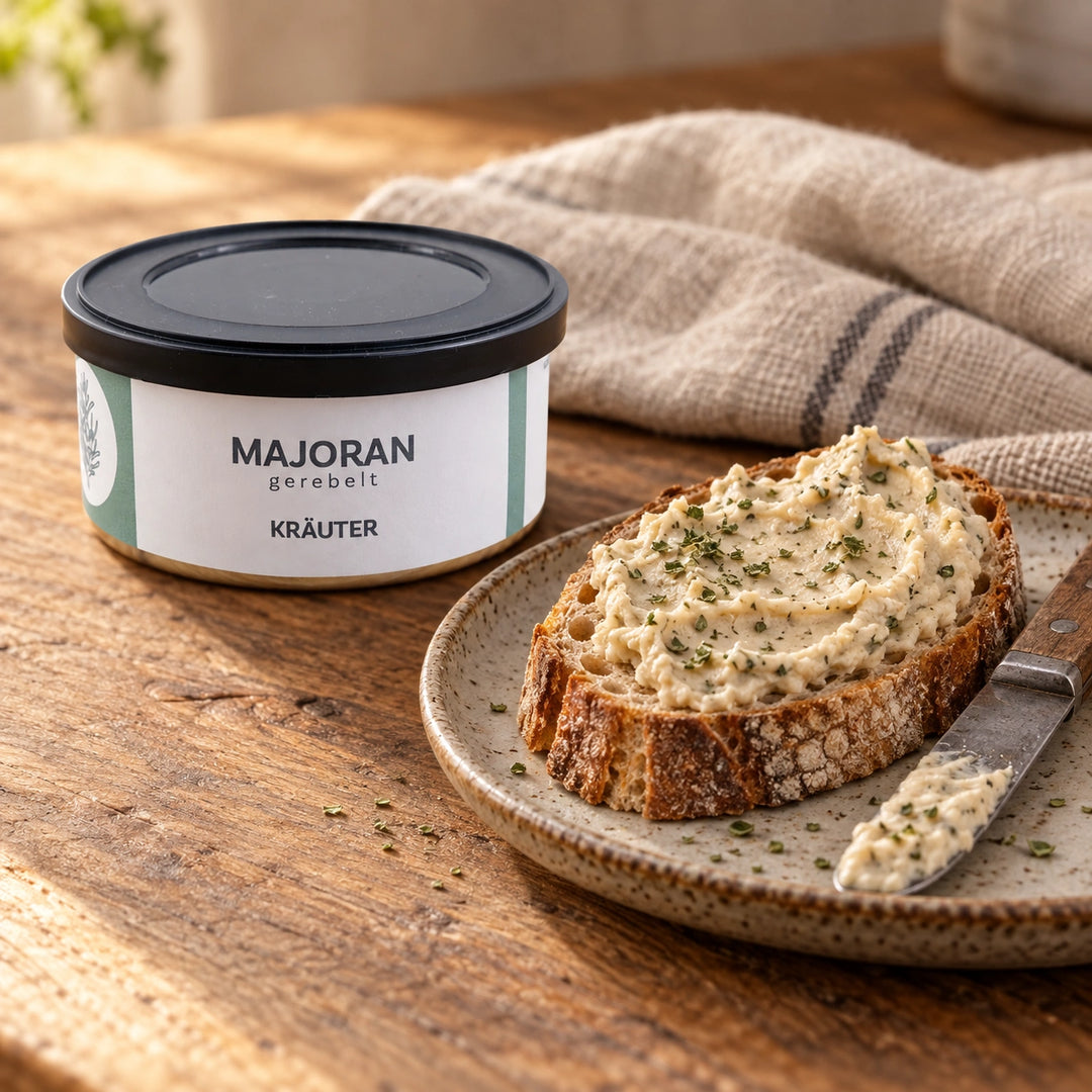 Majoran gerebelt von Jungermann Gourmet in der geschlossenen Dose neben einem Brot mit cremigem Kräuteraufstrich und einem bestrichenen Buttermesser