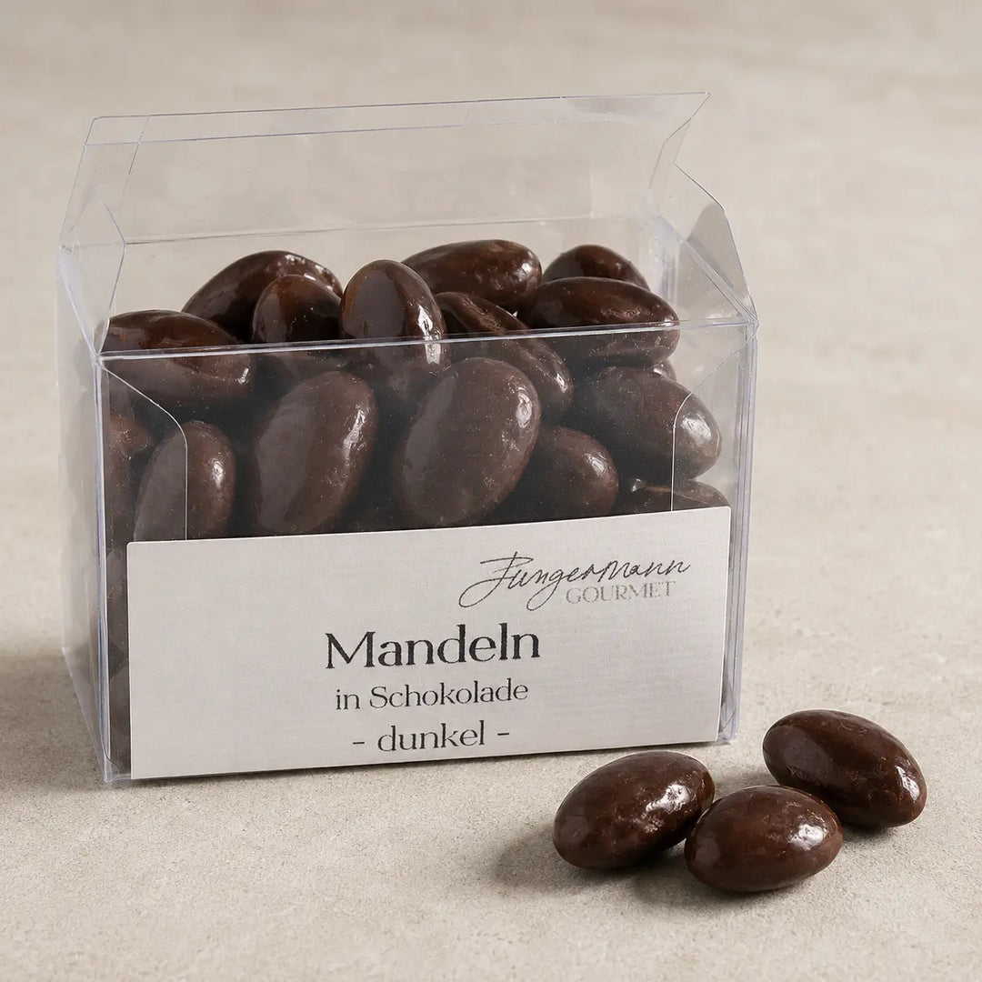 Geöffnete Klarsichtbox mit dunklen Mandeln in Schokolade