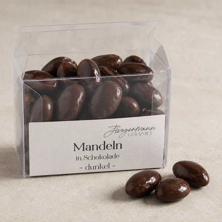 Geöffnete Klarsichtbox mit dunklen Mandeln in Schokolade