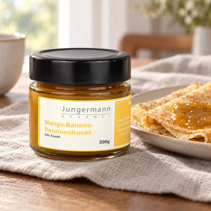 Mango-Banane-Passionsfrucht-Aufstrich von Jungermann Gourmet im Originalglas neben Crêpes mit Aufstrich als süßer Serviervorschlag.