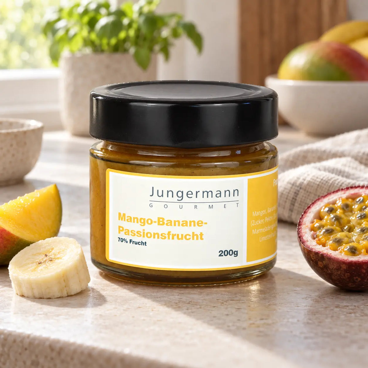 Mango-Banane-Passionsfrucht-Aufstrich von Jungermann Gourmet im Originalglas neben passenden Zutaten auf einer Küchenarbeitsplatte.