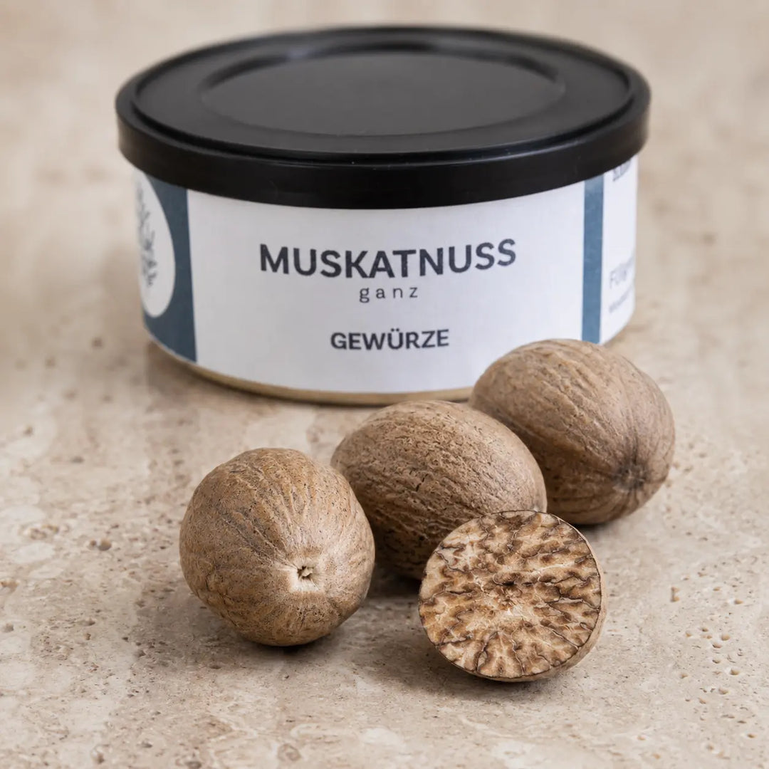 Ganze und aufgeschnittene Muskatnüsse im Detail vor der originalen Gewürzdose