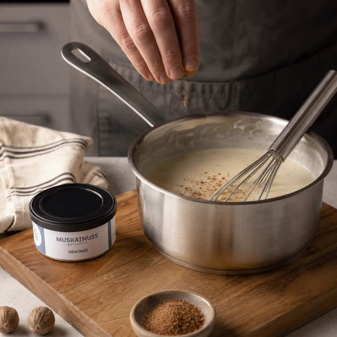 Gemahlene Muskatnuss wird in cremige Béchamelsauce gestreut neben der originalen Gewürzdose