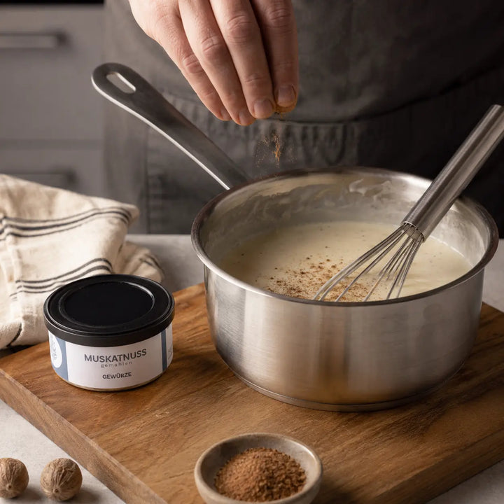 Gemahlene Muskatnuss wird in cremige Béchamelsauce gestreut neben der originalen Gewürzdose