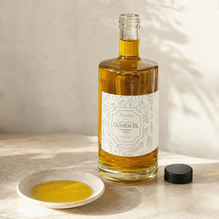 Geöffnete originale Olivenölflasche mit schwarzem Deckel und Olivenöl in einer Probenschale