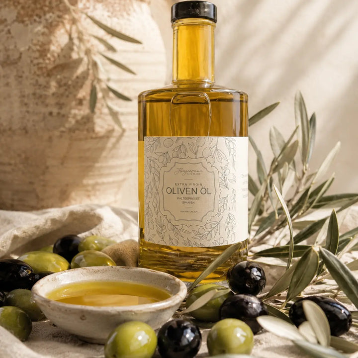Originale Olivenölflasche mit grünen und schwarzen Oliven, Olivenblättern und goldenem Öl