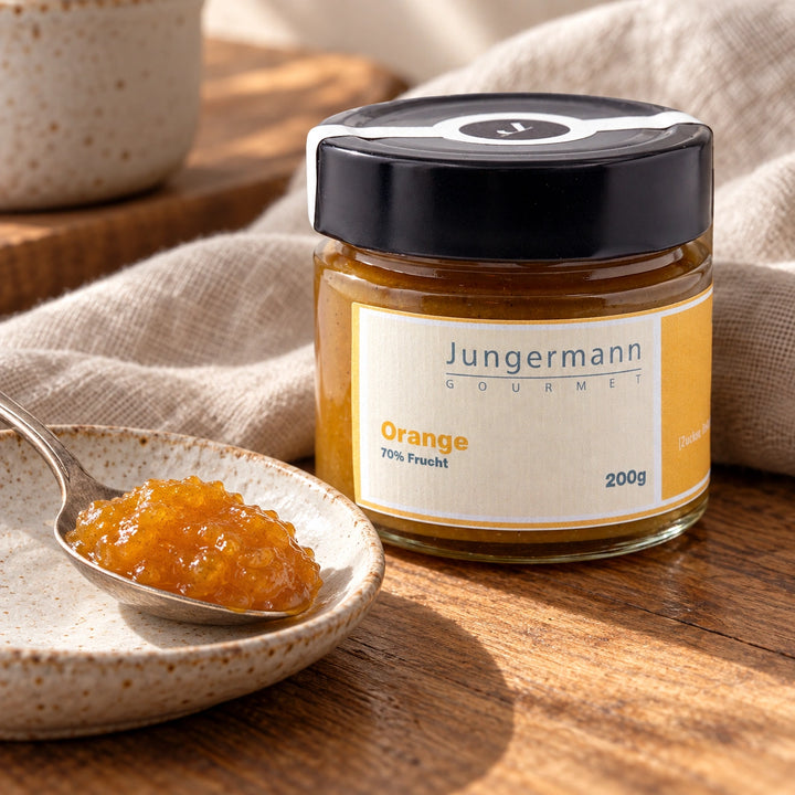 Orangenaufstrich auf einem Teelöffel und einer kleinen Keramikschale neben dem Originalglas.