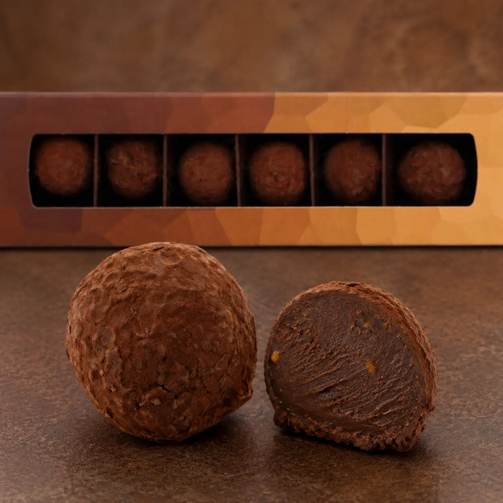 Orangen Trüffel im Anschnitt mit dunkler Ganache vor der originalen Sechserbox