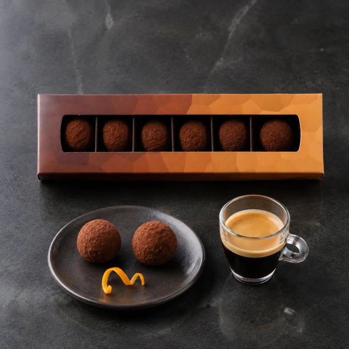 Zwei Orangen Trüffel zu Espresso neben der originalen Sechserbox