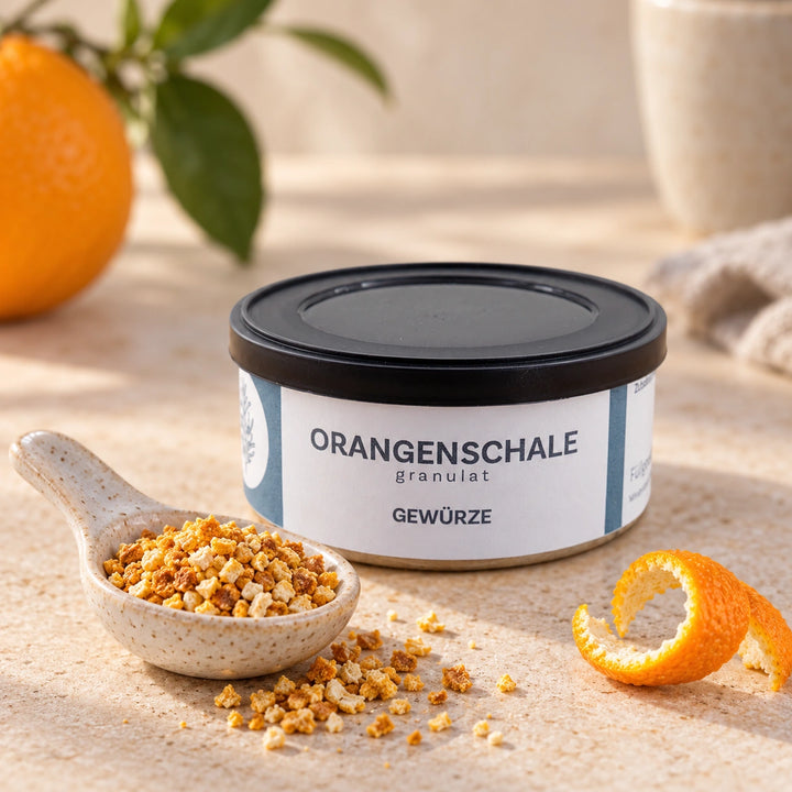 Orangenschalen-Granulat auf einem Keramiklöffel neben einer Orangenschale; die Originaldose ist vollständig mit lesbarem Etikett zu sehen.