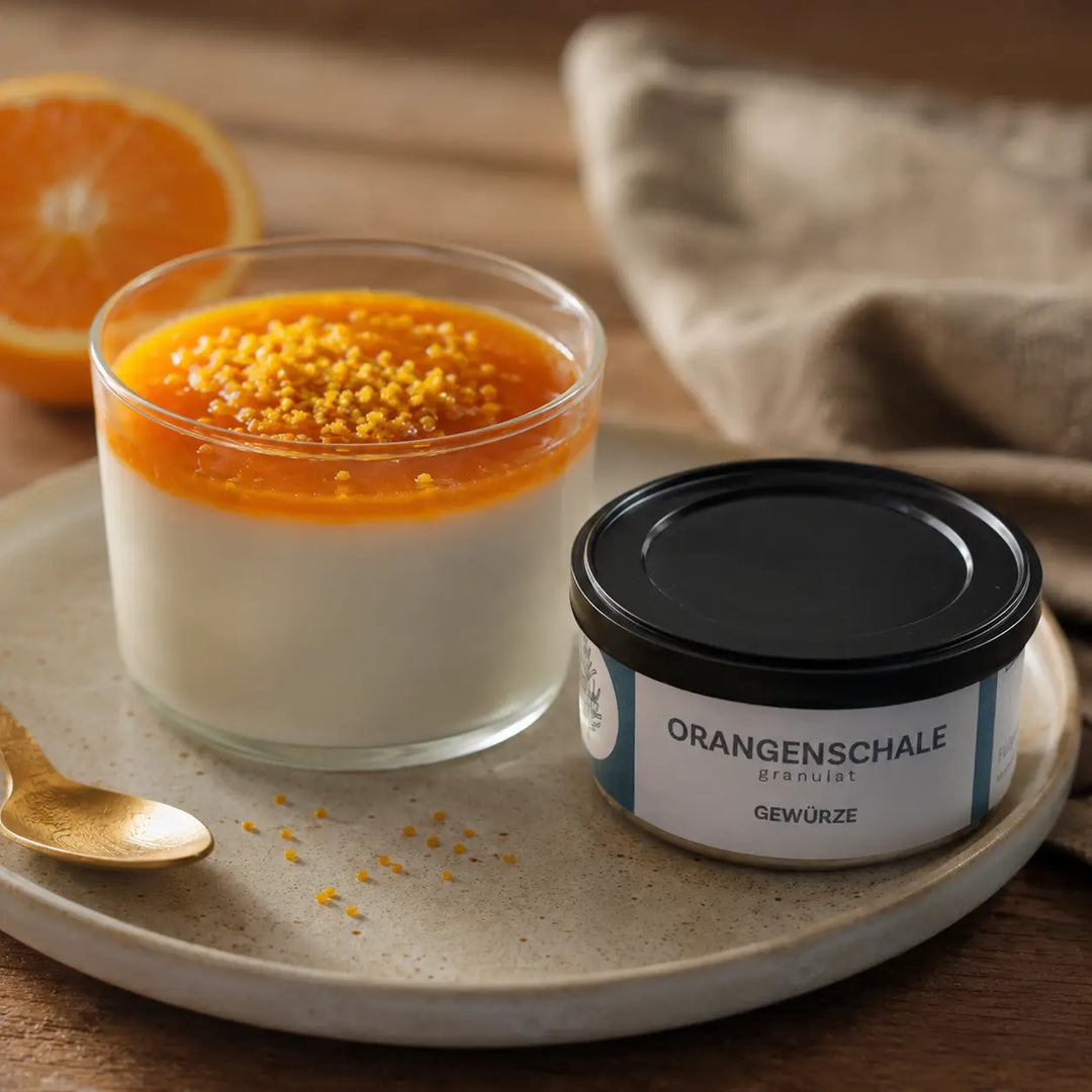 Panna cotta mit Orangensauce und Orangenschalen-Granulat neben der originalen Gewürzdose