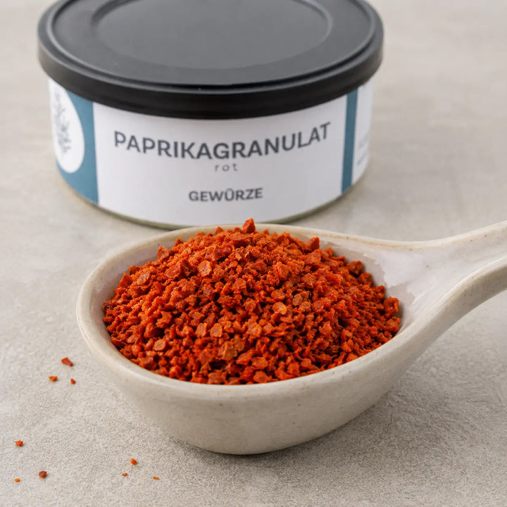 Grobes rotes Paprikagranulat im Detail vor der originalen Gewürzdose