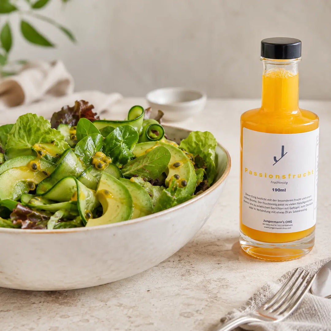 Frischer Salat mit Passionsfrucht-Dressing neben der originalen Essigflasche