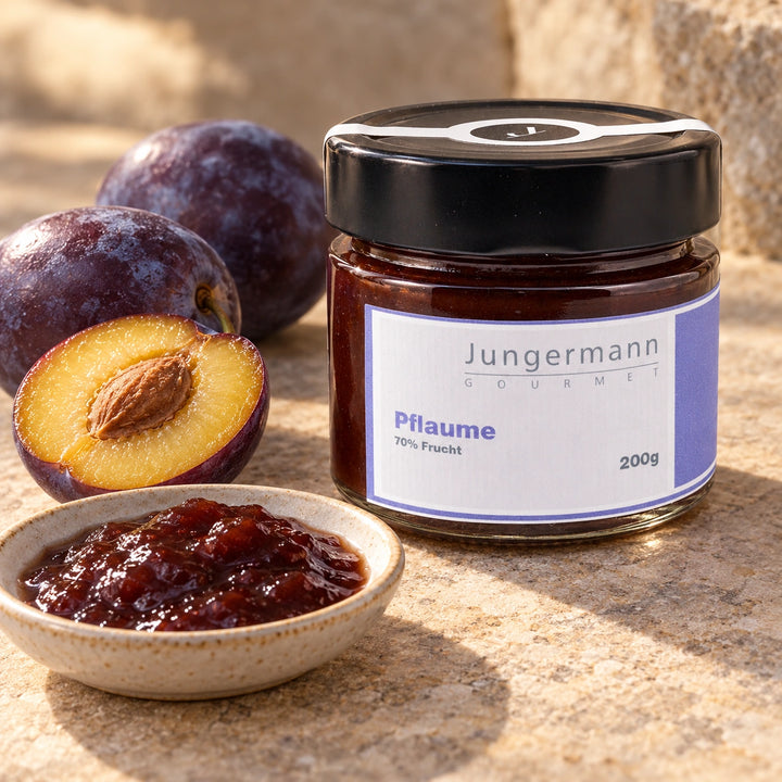 Reife Pflaumen, eine aufgeschnittene Frucht und Pflaumenaufstrich neben dem Originalglas.