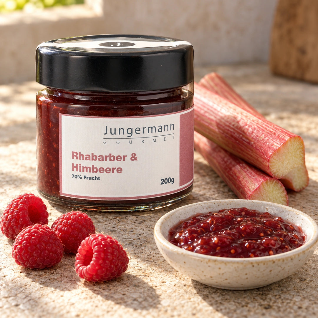 Rhabarberstangen und frische Himbeeren neben dem Originalglas des Fruchtaufstrichs.