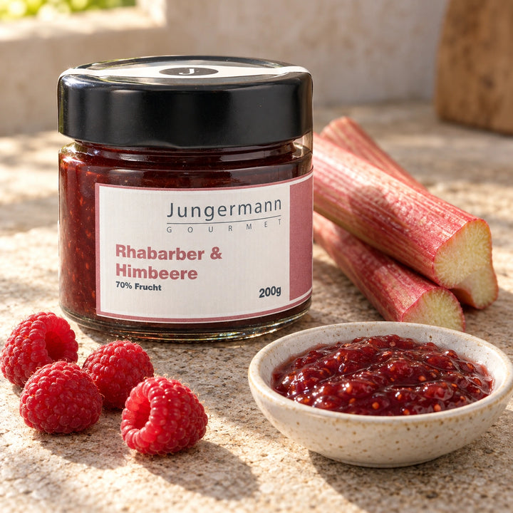 Rhabarberstangen und frische Himbeeren neben dem Originalglas des Fruchtaufstrichs.