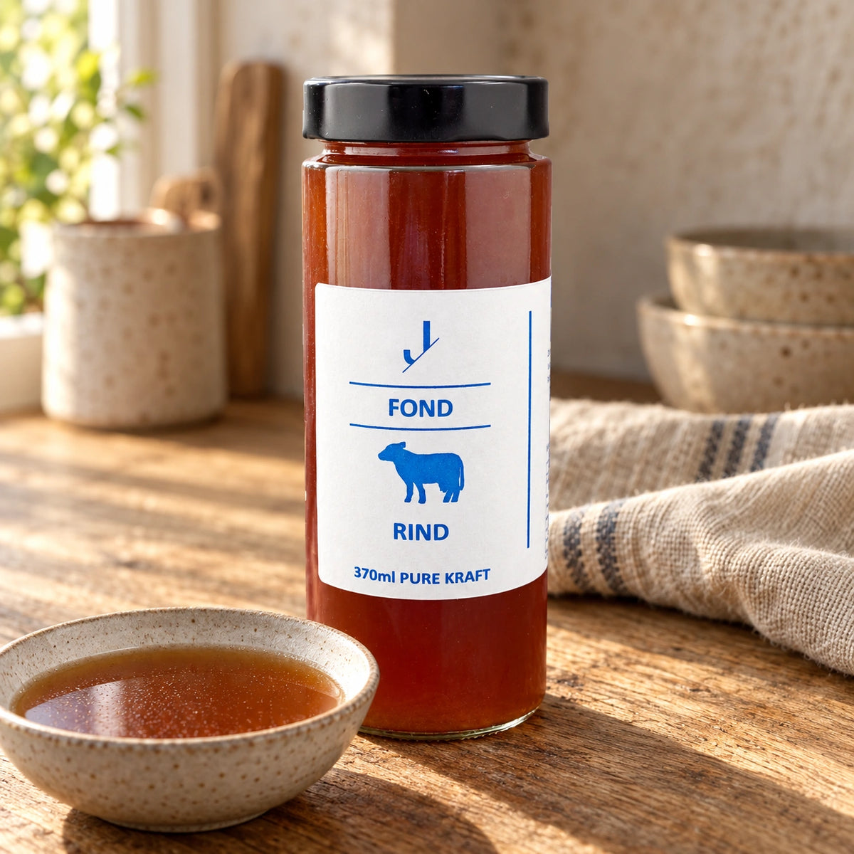 Rinder-Fond im originalen 370-ml-Glas neben einer kleinen Schale Brühe auf einem Holztisch.
