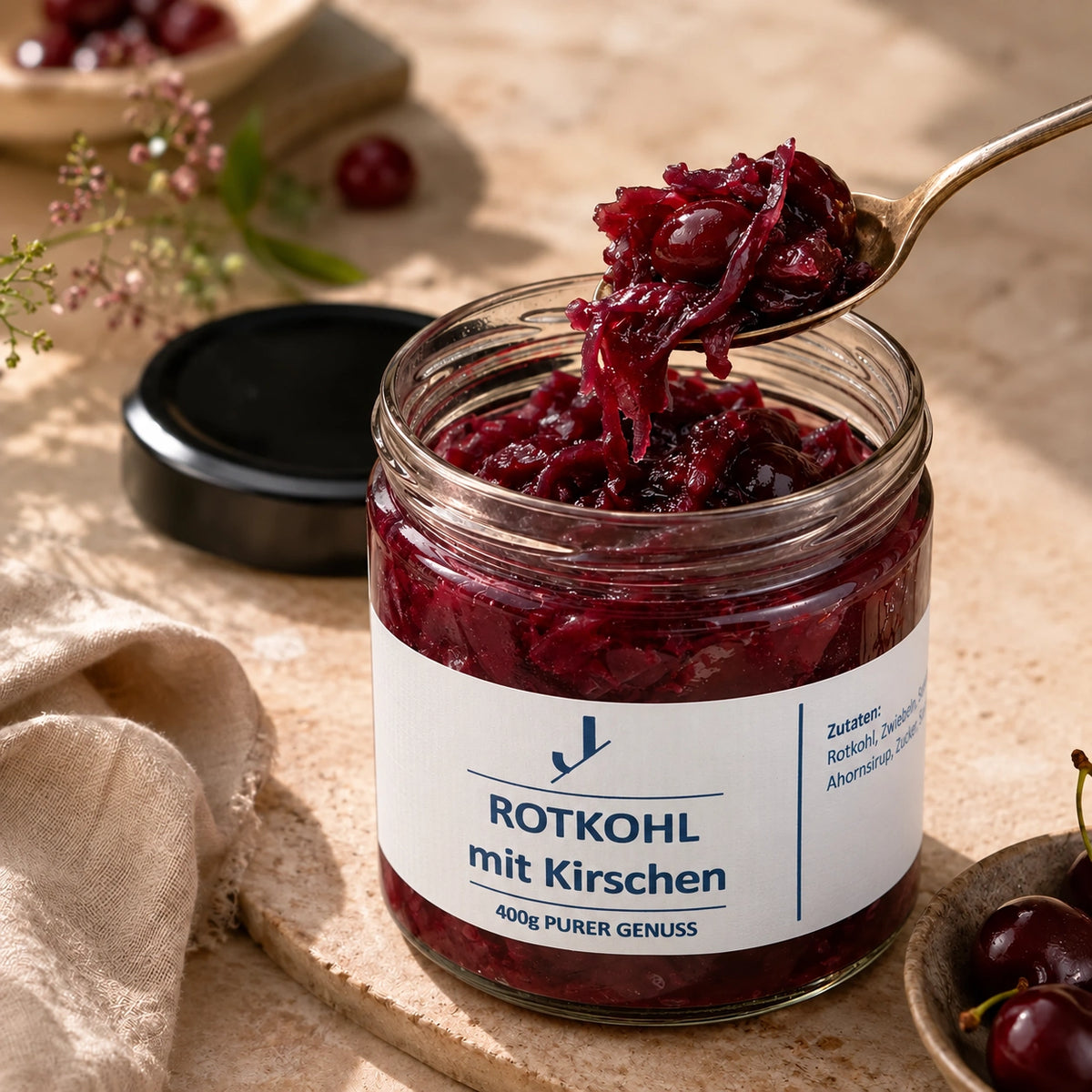 Rotkohl mit Kirschen im geöffneten Originalglas mit blauem Etikett und einem gefüllten Löffel.