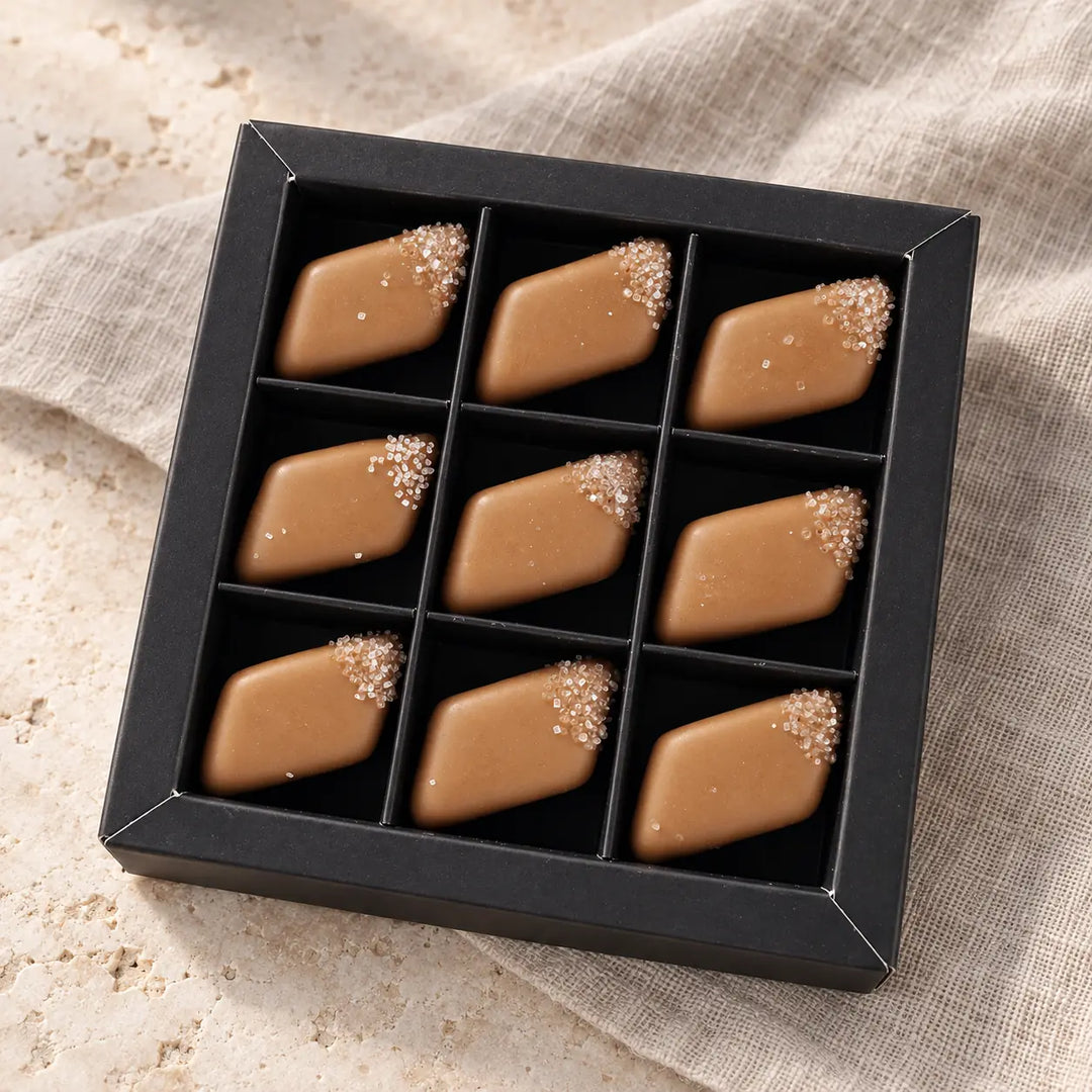 Neun karamellfarbene Salz-Karamell-Pralinen mit Salzdekor in der schwarzen Originalbox mit neun Einzelfächern.