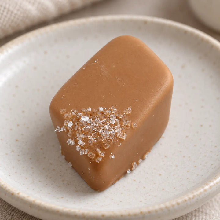 Nahaufnahme einer rautenförmigen Salz-Karamell-Praline mit heller Schokoladenhülle und Salzkristallen an einer Ecke.
