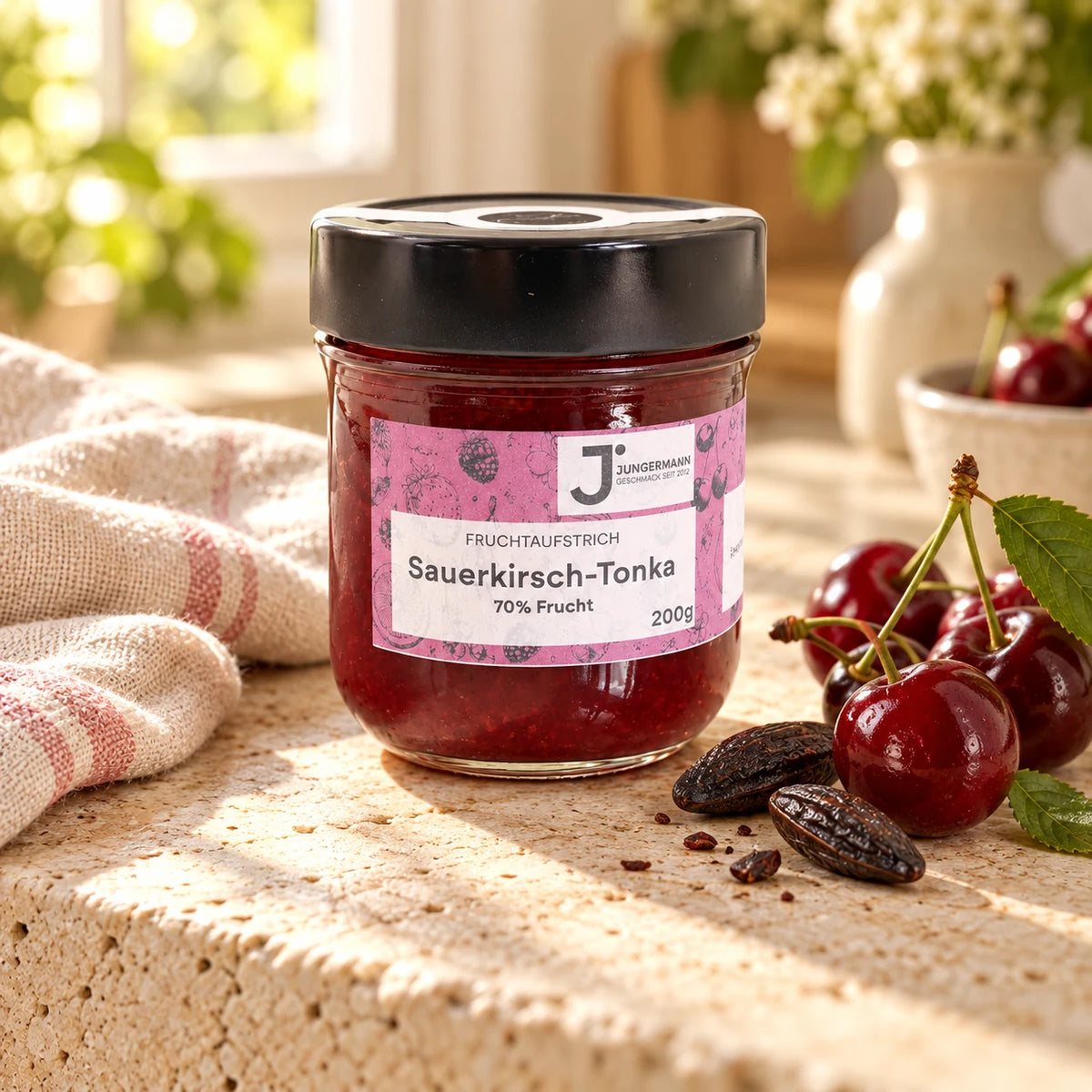 Sauerkirsch-Tonkabohnen Fruchtaufstrich von Jungermann Gourmet im 200-g-Glas auf hellem Naturstein mit Sauerkirschen und Tonkabohnen