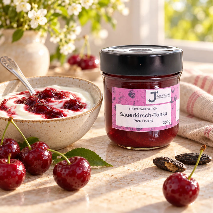 Serviervorschlag: Naturjoghurt mit Sauerkirsch-Tonkabohnen Fruchtaufstrich in einer Keramikschale neben dem Glas und Sauerkirschen
