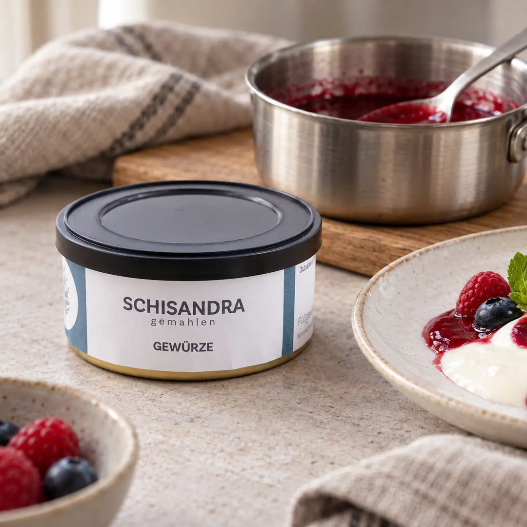 Schisandra gemahlen neben einem Topf Fruchtsauce und einem Beerendessert als Zubereitungs- und Serviervorschlag.